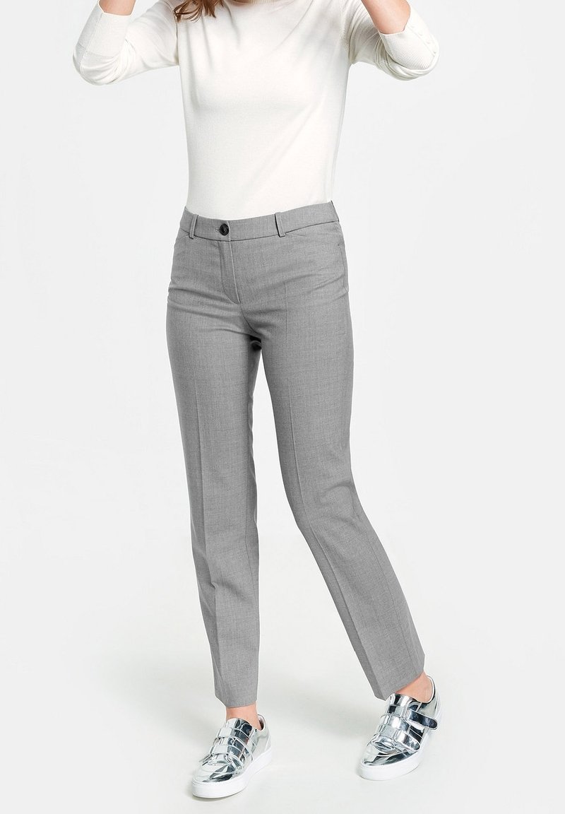 Pantalon gris sur mesure à texture lisse, jambes droites, fermeture à boutons sur le devant, porté avec des baskets argentées brillantes et un haut blanc.