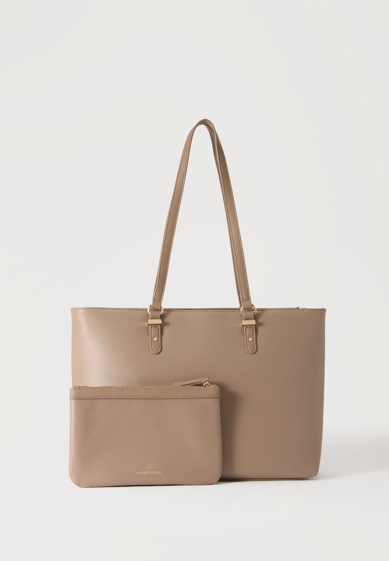 Sac cabas en cuir beige avec double anses et pochette assortie à fermeture éclair placée devant sur un fond blanc.