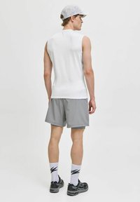 Ujjatlan fehér sporttop, szürke rövidnadrág, fekete cipő és fehér zokni fekete mintával. A modell hátulról látható, semleges háttérrel.