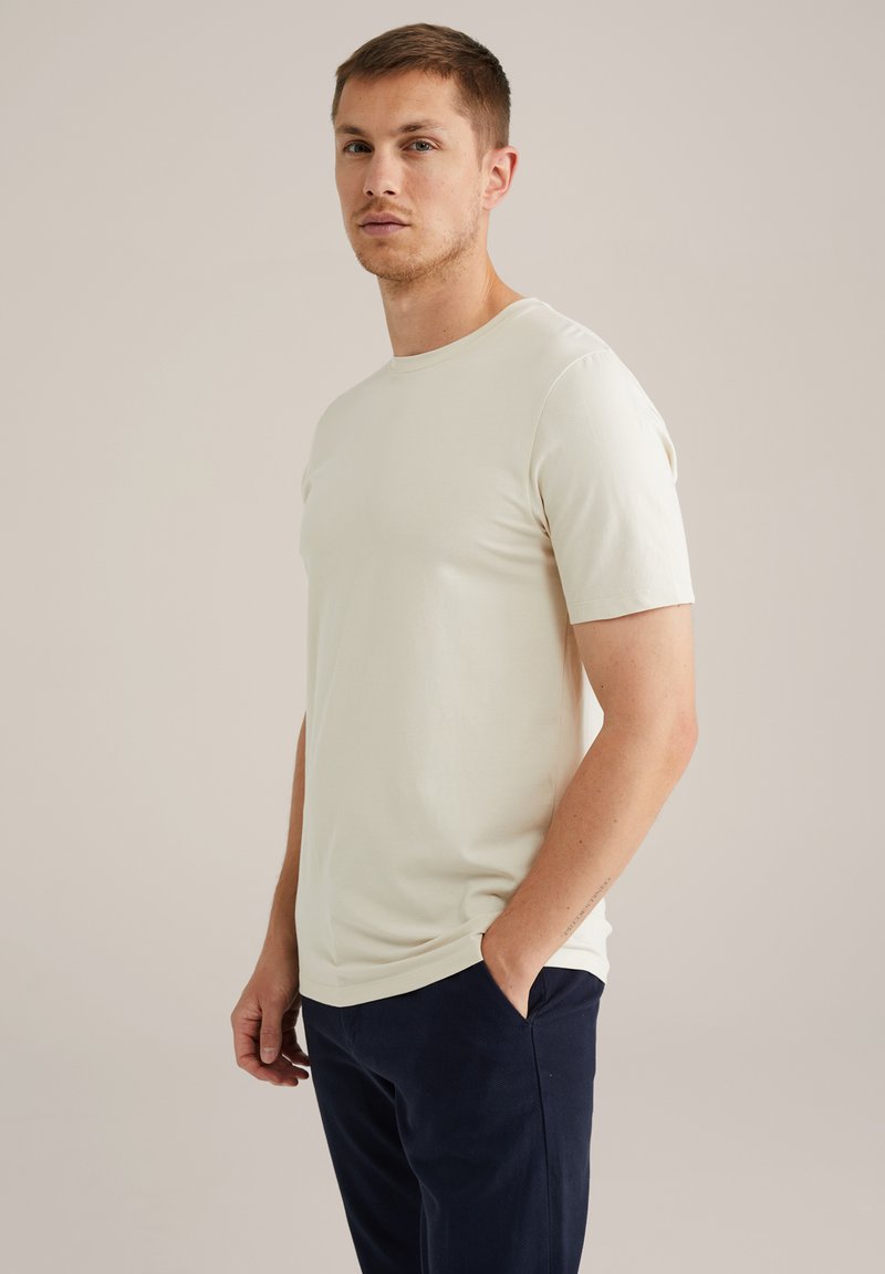 Tricou bej cu mânecă scurtă dintr-un material moale, cu un guler clasic tip crew, având o croială lejeră și o ușoară elasticitate. Purtați-l cu pantaloni bleumarin.