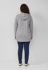 Grijze hoodie met lange mouwen en een capuchon, gemaakt van zachte stof. Gecombineerd met aansluitende donkerblauwe spijkerbroek en lichtgekleurde casual schoenen.