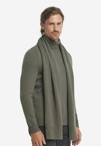 Olivengrønt strikket sweater med høj krave, parret med et matchende tørklæde. Ribbekantede ærmer og kant giver tekstur og detaljer.