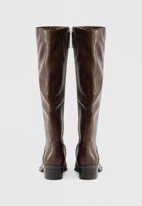 Brązowe skórzane cholewki do kolan o gładkiej fakturze, prostokątnym kształcie i niskim, klinowym obcasie; posiadają zamek błyskawiczny z tyłu oraz detale przeszycia.
