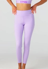 Woman wearing lavender high-waisted leggings and matching sports bra with PSD logo, standing with hands resting on hips.