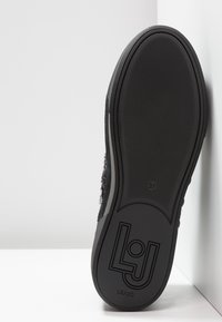 Svart sneaker med texturerad yta, gummisula och logotypdetalj. Har storlek 37 märkning på undersidan för identifiering.