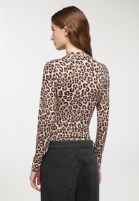 Top fitted a maniche lunghe di colore beige con stampa leopardata nera. Tessuto morbido con una texture liscia. Abbinato a pantaloni neri a vita alta.
