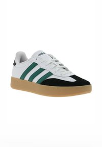 Sneaker bianca con accenti verdi e neri, caratterizzata da tre strisce verdi, una parte superiore morbida e testurizzata, e una suola in gomma color gomma.