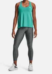 Top de entrenamiento color turquesa con tirantes, combinado con leggings ajustados grises de textura y zapatillas deportivas blancas.