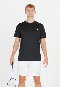 Svart tränings t-shirt med korta ärmar, med en liten vit "FZ" logotyp på vänster bröst. Bärs med vita shorts och håller en badmintonracket.