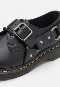 Scarpa in pelle nera con cinturino a fibbia, punta rotonda e suola in gomma. Presenta cuciture gialle e accenti in metallo silver.