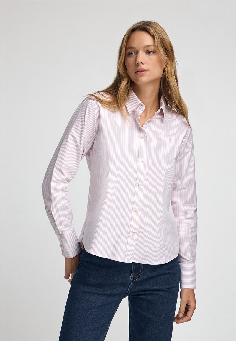Ljust rosa randig knäppt skjorta med krage, långa ärmar och smal passform. Har en liten logotyp på vänster bröst och pärlemorknappar.