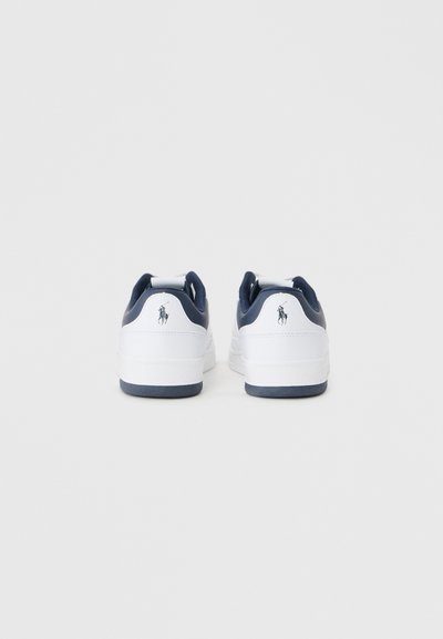 Tênis brancos com detalhes em azul-marinho, material semelhante a couro, sola plana e logótipo bordado no calcanhar. Design simples e desportivo com um acabamento texturizado.