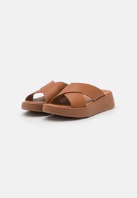 Sandali marroni con cinturini incrociati, dotati di suola a zeppa, realizzati in materiale sintetico liscio, con una soletta testurizzata per il comfort.