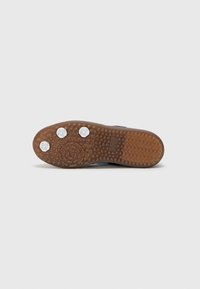 Sport shoe outsole featuring a textured rubber bottom in brown, with circular and hexagonal patterns, and three white circular studs.