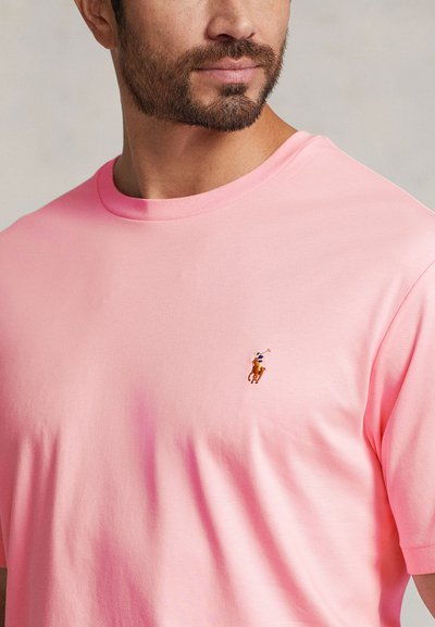 Różowy bawełniany t-shirt z okrągłym dekoltem, z małym, haftowanym logo konia na lewej piersi. Gładka faktura, krótkie rękawy.