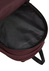 Mochila marrón con una abertura con cremallera, que muestra un interior liso de color negro. Cuenta con tela duradera y correas de hombro acolchadas.