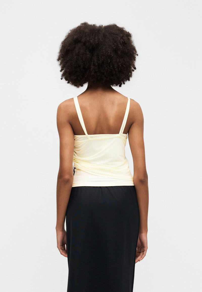 Haut débardeur jaune clair froncé avec fines bretelles, associé à une jupe noire. Le tissu paraît doux et lisse, avec une coupe moulante.