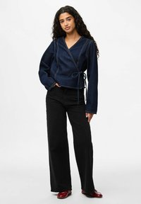 Top in denim con maniche lunghe, scollo a V profondo e dettagli di cucitura visibili; abbinato a pantaloni neri a vita alta e a gamba larga e scarpe bordeaux.