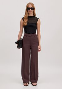 Zwarte aansluitende top, wijde donker bordeauxrode broek, oversized zwarte clutch en zwarte zonnebril. Gladde stof met een strak ontwerp.