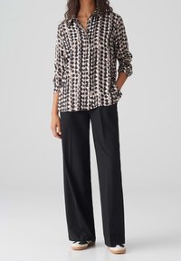 Long-sleeve shirt in beige with black and white polka dot print, paired with black wide-leg pants and black sneakers with white accents.
