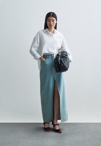 Ljusblå denim maxikjol med en framklippt slits, parat med en vit randig skjorta med knäppning och röda högklackade skor. Tillbehören inkluderar en svart väska.