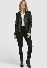 Black leather biker jacket with zip details, fitted black leggings, and ankle boots. Light-colored button-up shirt underneath.