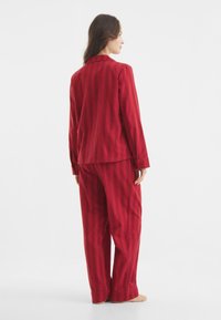 Punainen raidallinen pyjaman setti, joka on valmistettu pehmeästä kankaasta. Takissa on kaulus ja pitkät hihat; housut ovat löysät ja suoranmalliset.