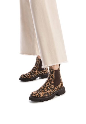 Botas de tobillo con estampado de leopardo, paneles laterales elásticos, parte superior texturizada, suela de goma negra y borde en zigzag. Llevadas con jeans cortos de color claro.
