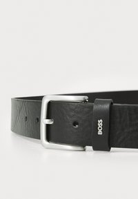 Black leather belt with a silver rectangular buckle and a texture detail. Features a branding tag embossed with "BOSS."