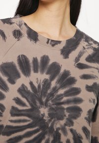 Tie-dye sweatshirt i beige och svart. Cirkulärt mönster med varierande nyanser. Rund halsringning och strukturerad bomullstextil.
