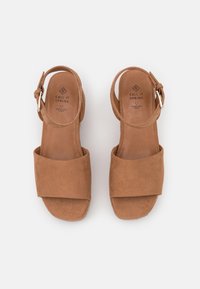 Sandales marron à bout ouvert avec larges brides avant et brides de cheville équipées de boucles métalliques, étiquetées "Call It Spring" et "véganes et durables."