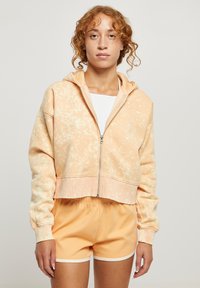 Felpa corta con zip in un morbido arancione con motivo tie-dye, dotata di cappuccio e orlo a costine. Abbinata a pantaloni corti arancioni coordinati.