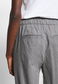 Szare teksturowane spodnie z elastycznym paskiem, dwoma tylnymi kieszeniami i luźnym krojem, przedstawione z tyłu z białą koszulą na górze.