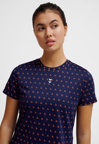 Mörkblå t-shirt i mjukt tyg med ett heltäckande orange mönster och en vit logodetalj. Kort ärm och rund halsringning.