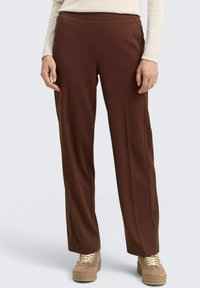 Braune, weit geschnittene Hosen aus glattem Stoff, mit einer mittelhohen Taille und Fronttaschen. Kombiniert mit beigen Schuhen.