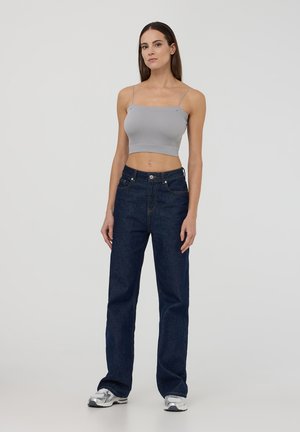 Top corto grigio a coste, jeans dritti blu scuro, sneakers argento. Spalline sottili sul top, design semplice dei jeans con cinque tasche.