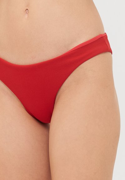 Sarkans bikini apakšējais daļa ar zemu jostu un plānām sānu siksnām, izgatavots no mīksta, gluda auduma. Rāda minimālu segumu un bez rakstiem.