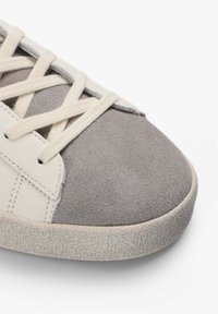 Zapatillas de ante gris y piel blanca con cordones crema, punta redondeada y suela de goma texturizada con un acabado estampado.