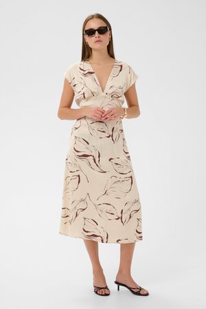 Beige blomsterkjole med brune bladmønstre, kappelignende ærmer og en dyb V-udskæring. Kjolen er midt på læggen og lavet af glat stof med et flydende design.