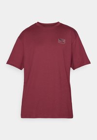 Bordeaux T-shirt, korte ærmer, rund halsudskæring, med et lille grafisk tryk på venstre bryst i kontrastfarver. Blødt, glat stof.