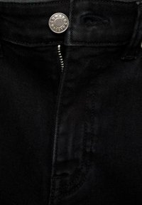 Gros plan d'un jean en denim noir avec un bouton argenté et une fermeture éclair argentée partiellement ouverte à la taille.