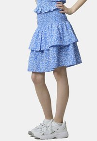 Gonna a balze blu con stampa floreale, vita arricciata e orlo volants, abbinata a sneaker sportive bianche. Il tessuto presenta un motivo leggero e strutturato.