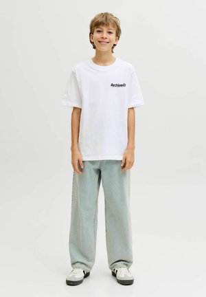 Valge puuvillane T-särk musta "Archive©" kirjaga rinnal, kombineeritud helesiniste laiade teksade ja mustvalgete tossudega.