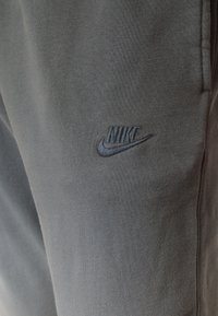 Pantaloni sportivi in cotone grigi con logo Nike ricamato in nero sul davanti. Tessuto morbido, dotati di tasche laterali e vita elastica.