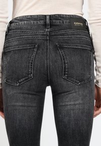 Schwarze Denim-Jeans mit hoher Taille, ausgestattet mit Gesäßtaschen, dezenten Used-Effekten und einem geprägten Lederetikett. Die Textur wirkt weich und abgenutzt.