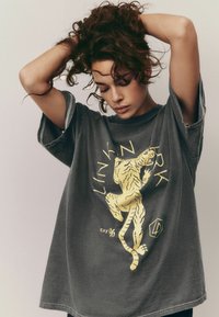 T-shirt surdimensionné gris avec un graphique de tigre jaune et du texte. Manches courtes avec revers, coupe décontractée et texture douce en coton.