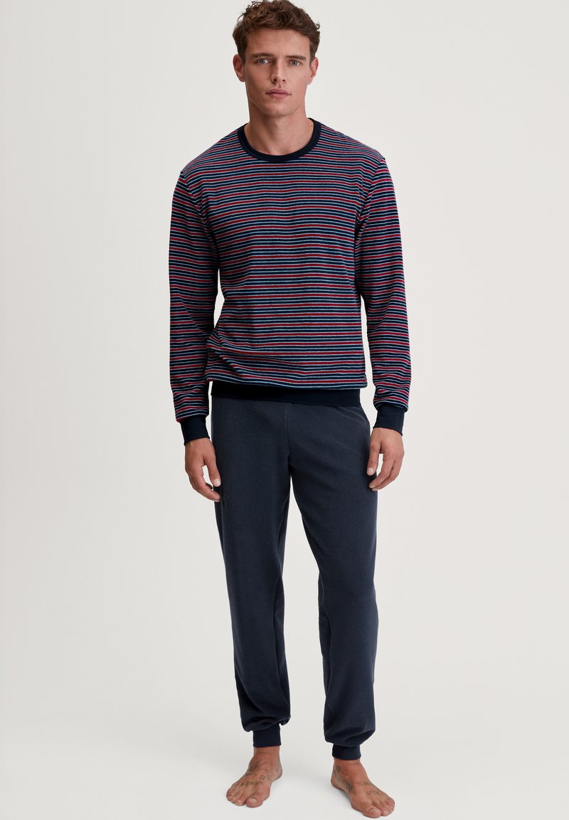 Chemise à rayures navy à manches longues avec des rayures rouges, bleues et blanches, associée à un pantalon de jogging court gris foncé, doté de poignets élastiques.
