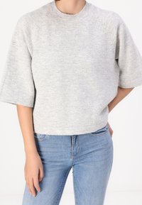 Pullover grigio a maniche corte in maglia con colletto a girocollo a coste, caratterizzato da una texture morbida e una vestibilità rilassata. Abbinato a jeans blu.