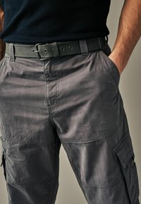 Graue Cargo-Hosen aus leichtem Material, mit Seitentaschen, lockerer Passform und einem strukturierten schwarzen Gürtel mit einer Metallschnalle.