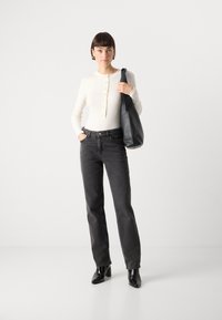 Top blanc à rayures, à manches longues, avec des boutons, associé à un jean noir taille haute et des bottines noires à talons pointus, le tout complété par un sac à main noir décontracté.